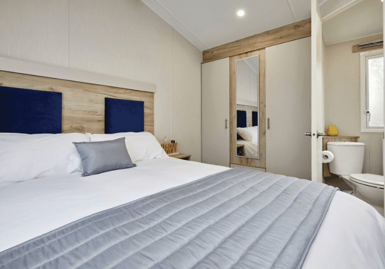 The Willerby Linwood master bedroom has a large wardrobe with a mirror, and has a upholstered dark blue headboard.