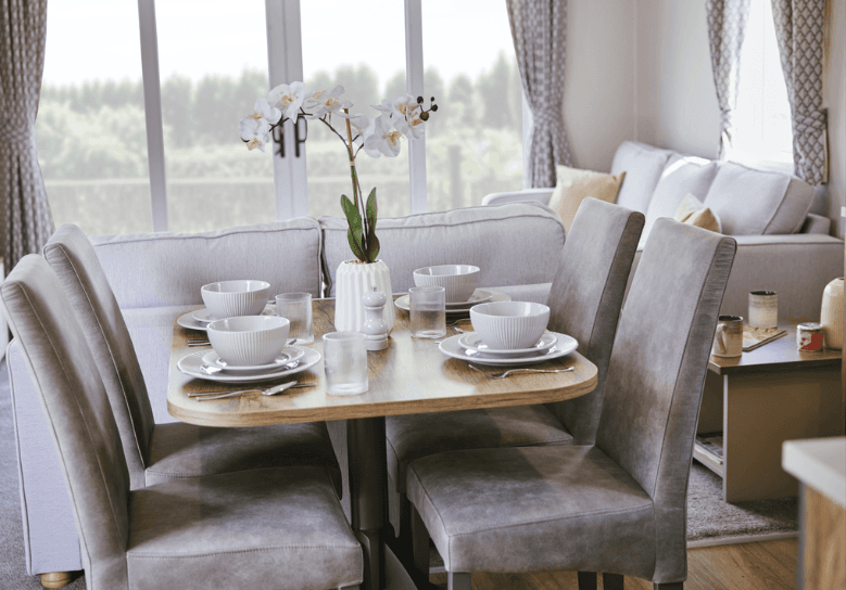 The Willerby Malton dining area has 4 grey chairs surrounding an oak effect table with white crockery and a centerpiece.