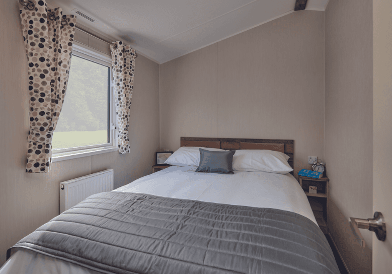 The Willerby Malton master bedroom has an upholstered pink headboard and spotted pink and grey curtains.