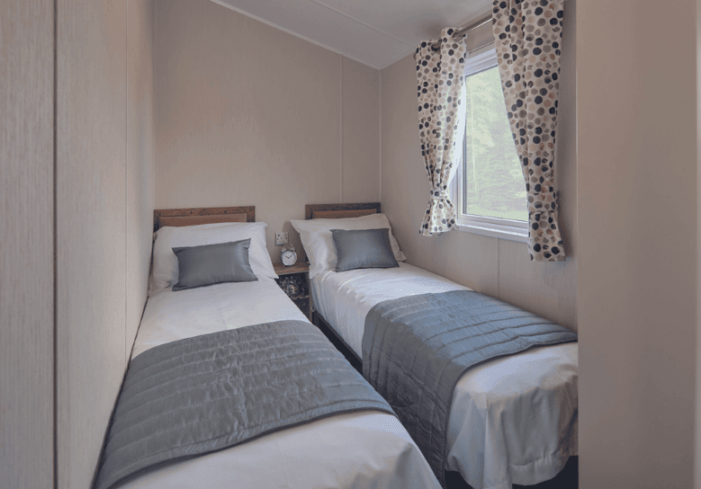 The Willerby Malton twin bedroom with a cream and oak effect wardrobe and spotted pink and grey curtains.