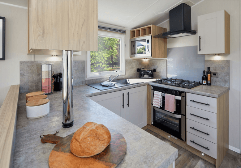 The Willerby Manor C-shaped kitchen has white cupboard doors on oak effect units and grey worktops.