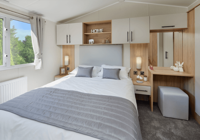 The Willerby Manor master bedroom has oak effect storage units and a dressing area with white cupboard doors.