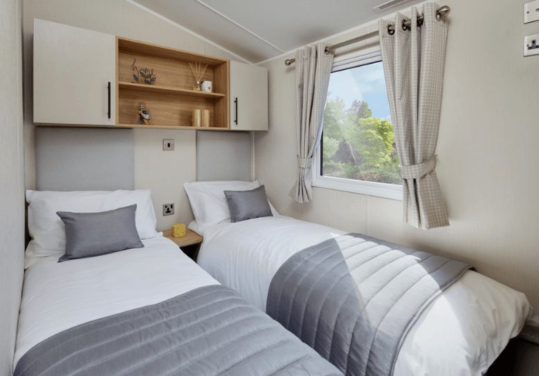 The Willerby Manor twin bedroom has oak effect storage units with white cupboard doors, and has a grey upholstered headboard.