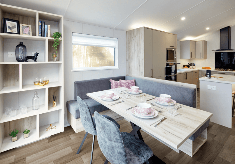 The Willerby Mapleton dining area has fixed and freestanding grey seating with storage underneath, and a white shelving unit next to the table.