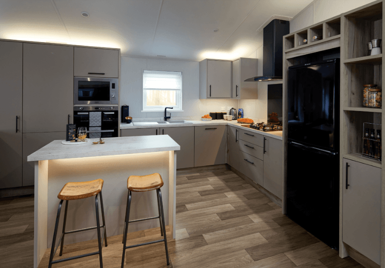 The Willerby Mapleton L-shaped kitchen has cream cupboard doors and white marble worktops, and a matching kitchen island with dark oak effect stools.