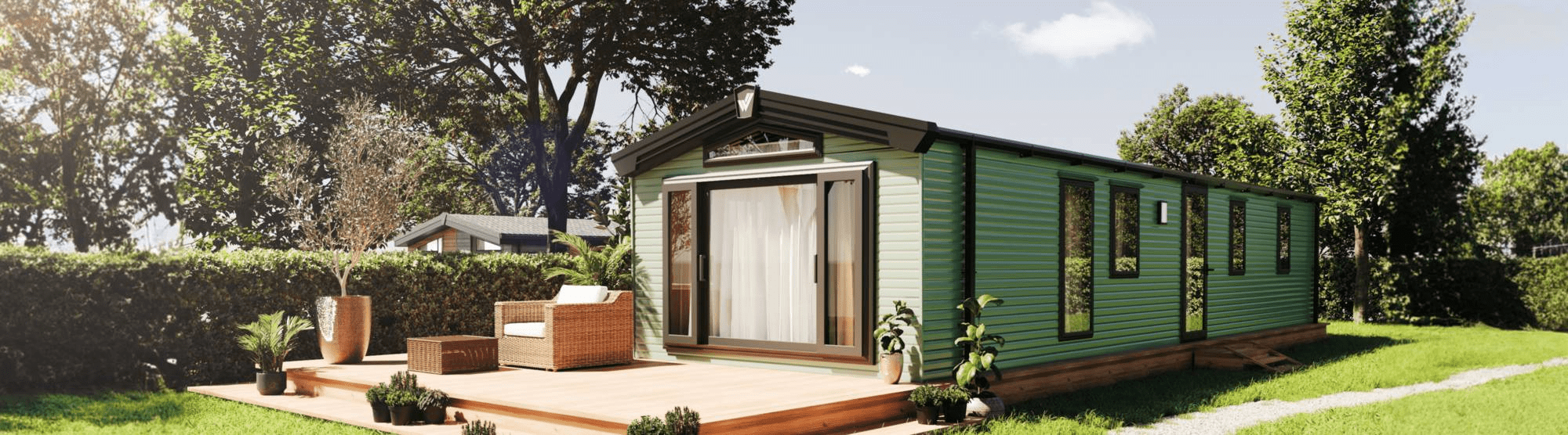 The Willerby Buxton holiday home on a grassy park with wooden decking. It has large windows at the front and is clad in a stylish sage green colour. 