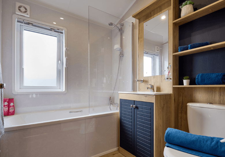 The Willerby New Holland bathroom has oak effect and deep blue storage units and a bathtub, matching the colour scheme of the lodge.
