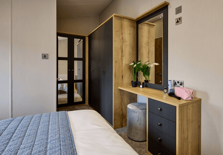 The Willerby New Holland dressing area has oak effect storage units and deep blue cupboard doors.