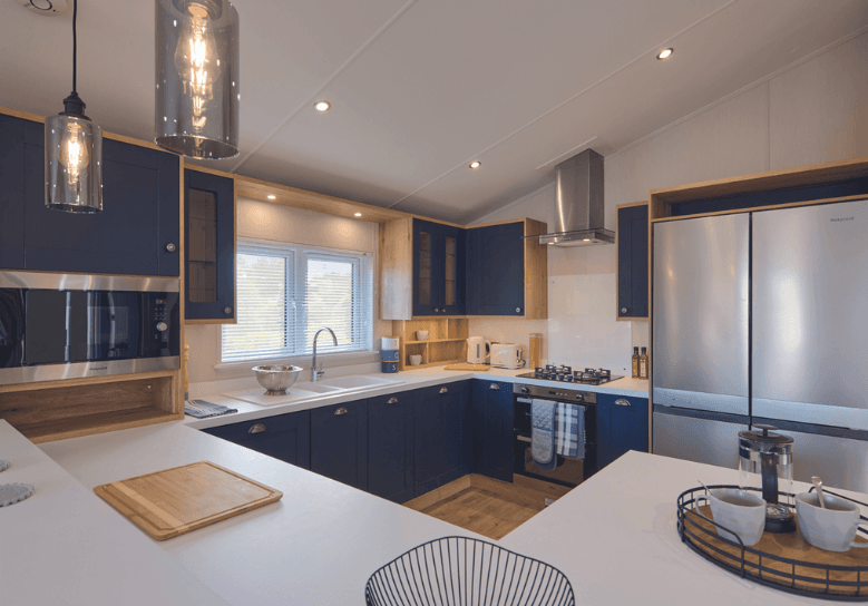 The Willerby New Holland G-shaped kitchen has white worktops and deep blue cupboard doors.