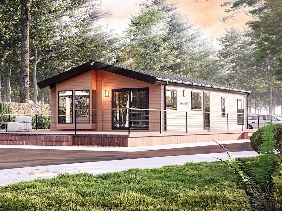 The Willerby Portland exterior in brown with brown decking sited on a grassy field with a forest behind.