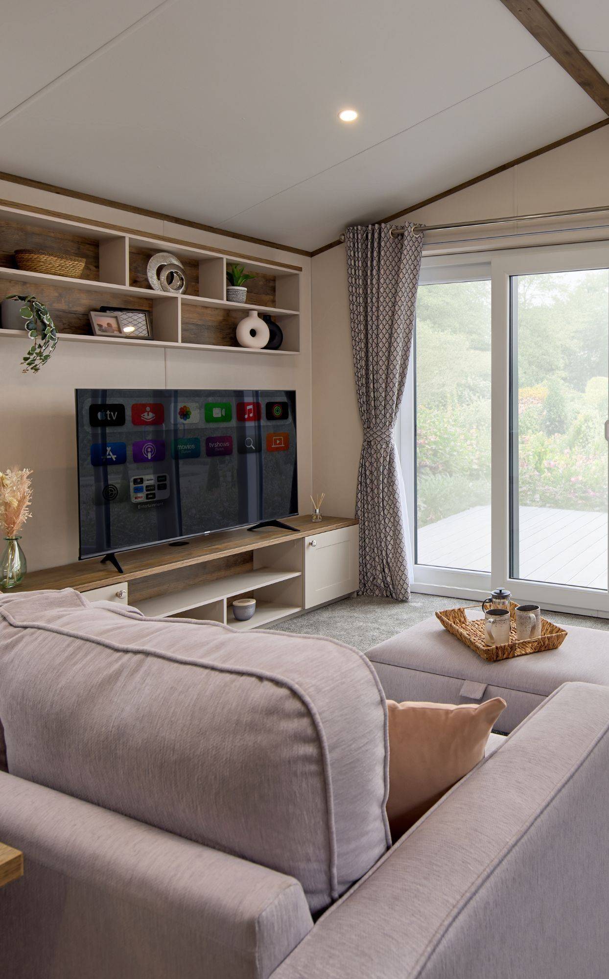 The Willerby Malton Elite spacious lounge with two grey free-standing sofas and a matching footstool with a storage media unit in cream and a dark oak effect.