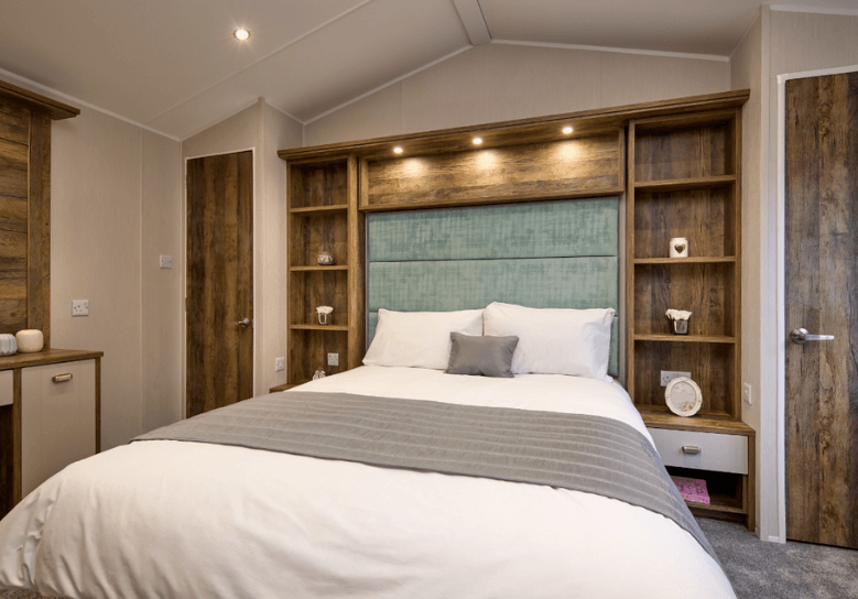 The Willerby Sheraton main bedroom has a green upholstered headboard surrounded by dark oak effect storage shelves.