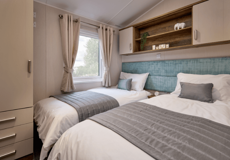 The Willerby Sheraton twin bedroom has green upholstered headboards, and a wardrobe and overhead storage in dark oak effect with white cupboard doors.