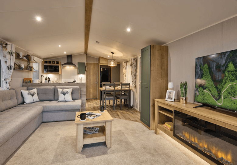 The Willerby Sierra lounge has a grey fixed L-shaped sofa with a small oak effect coffee table in the center, and a large oak effect media unit with an electric fire.