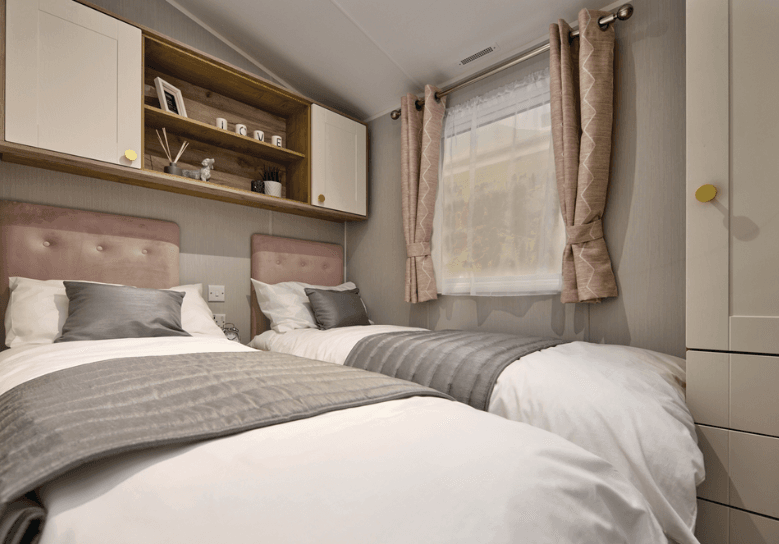 The Willerby Sierra twin bedroom has oak effect storage units with white cupboard doors, and pink upholstered headboards and matching curtains.