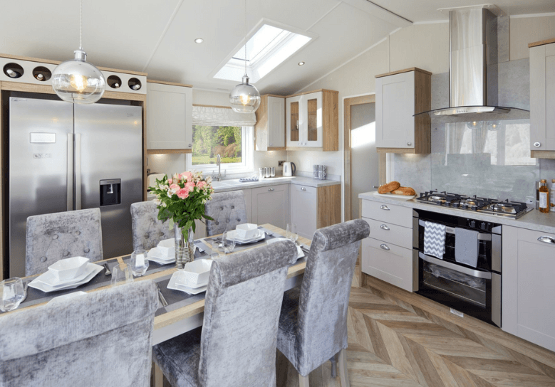 The Willerby Vogue Classique kitchen has oak effect storage units with white cupboard doors, and a luxurious oak effect and grey dining table with grey dining chairs surrounding.