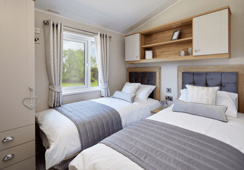 The Willerby Vogue Classique twin bedroom has oak effect storage units with white cupboard doors, and grey upholstered headboards.