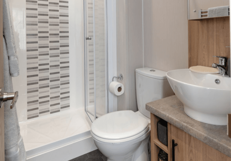 The Willerby Waverley bathroom has oak effect storage units and a shower with a textured wall.