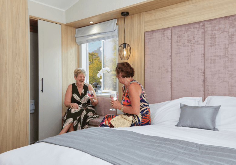 The Willerby Waverley master bedroom has a tall pink upholstered headboard with oak effect storage units.