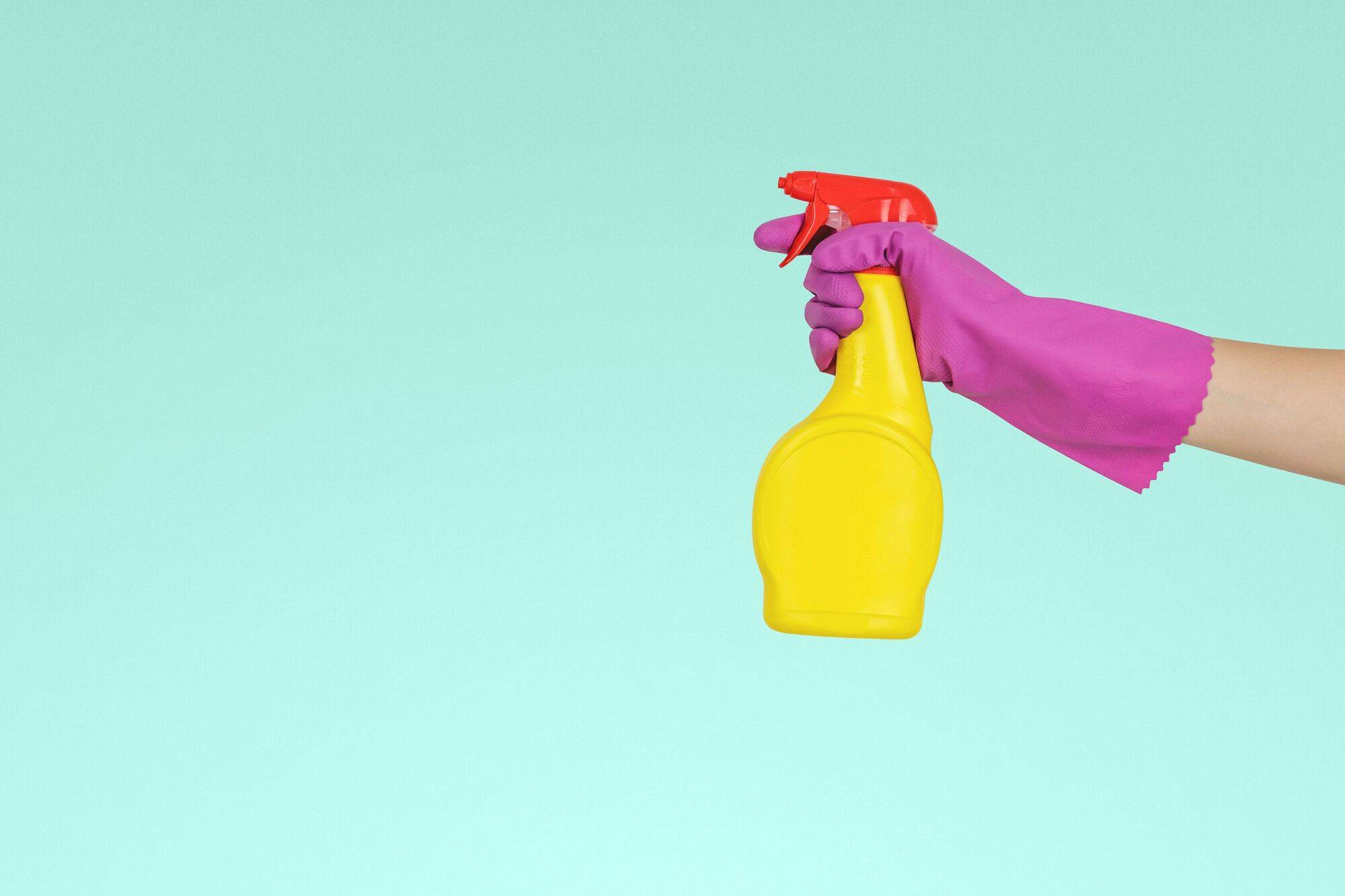 Hand in pink cleaning glove holding yellow cleaning spray