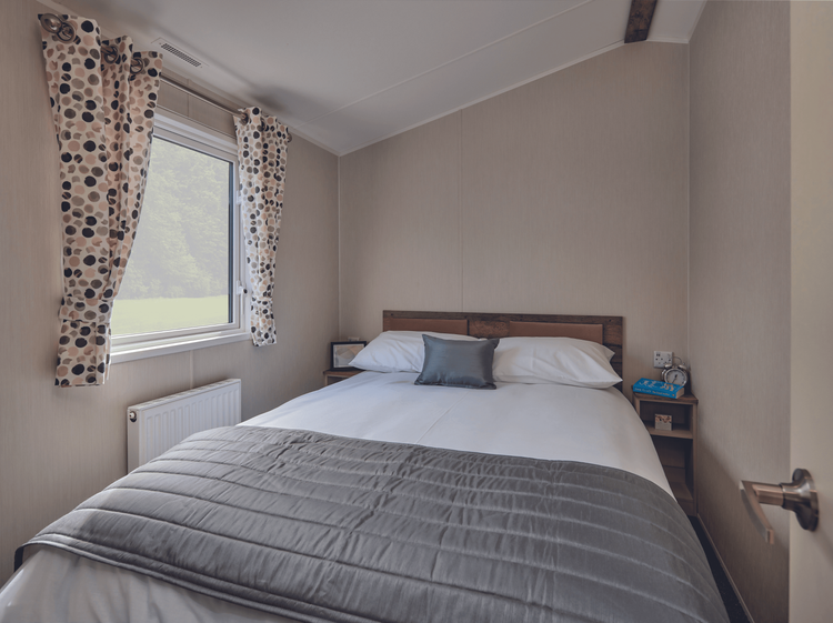 The Willerby Malton master bedroom has an upholstered pink headboard and spotted pink and grey curtains.