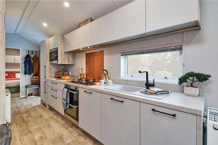 The Willerby Astoria stylish linear kitchen with white cupboard doors and an orange splashback.