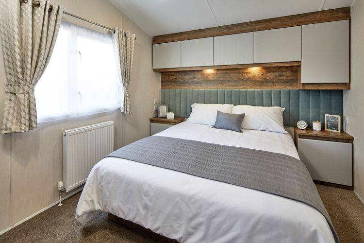 The Willerby Brookwood calming master bedroom with overhead storage with white cupboard doors and an upholstered sage green headboard.