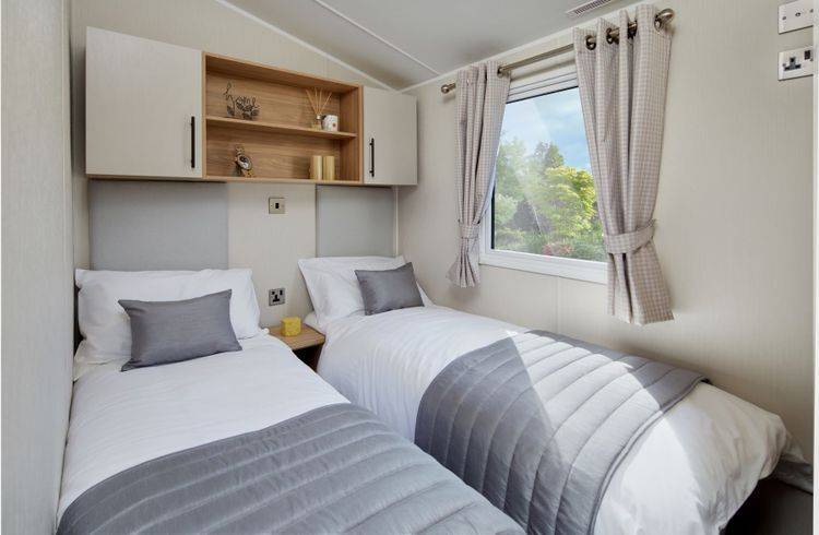 The Willerby Manor twin bedroom has oak effect storage units with white cupboard doors, and has a grey upholstered headboard.