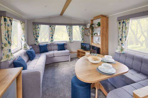The Willerby Ashurst lounge adorned with grey corner seating for both lounge and diner, and blue pillows matching the stool and curtains.