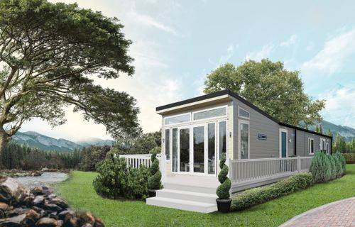 The Willerby Vogue Classique is a spectacular luxury holiday home with a distinctive sloped front end. It's sited on a grassy pitch with a stream and mountains in the background. 