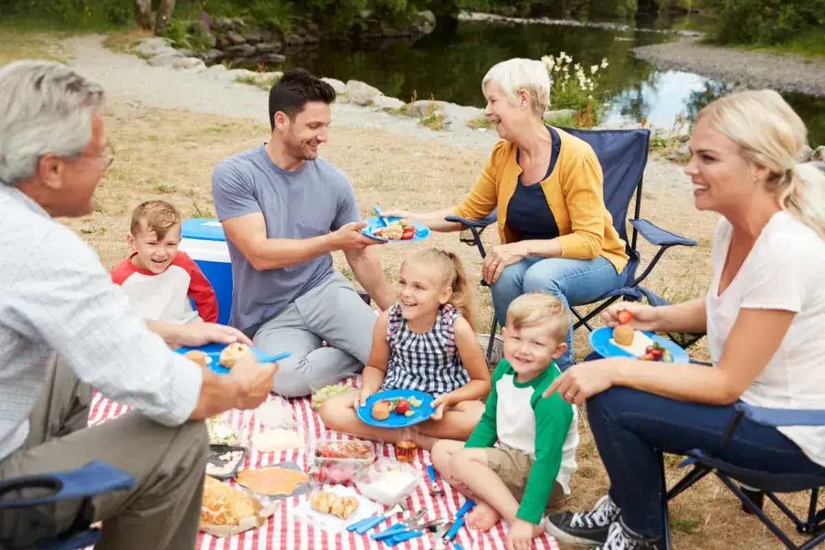 Grandparents, parents and children sat on a red checked blanket enjoying a picnic