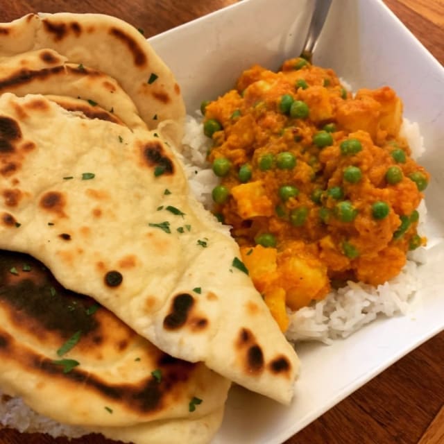 Several torn-off peices of naan atop a bowl of rice and aloo paneer.