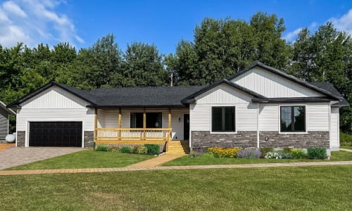 Modern white ranch-style home with black trim, large black windows, a covered porch, stone accents, and colorful front landscaping on a well-kept lawn.