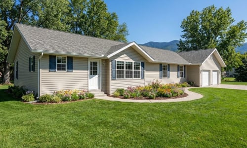 Beige modular ranch home with blue shutters, attached garage, and flower landscaping by Wisconsin Homes in Marshfield, WI.