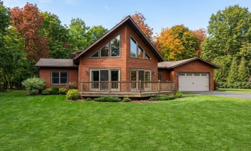 Cedar-toned Chalet-style modular home by Wisconsin Homes in Marshfield, WI with large windows and attached garage.