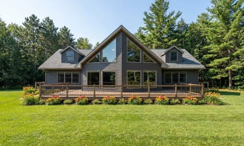 Gray Chalet-style modular home by Wisconsin Homes in Marshfield, WI with full front deck and floor-to-ceiling windows.