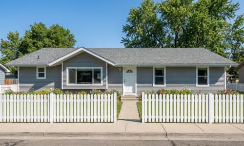 Gray modular ranch home with white picket fence and flower beds by Wisconsin Homes in Marshfield, WI.