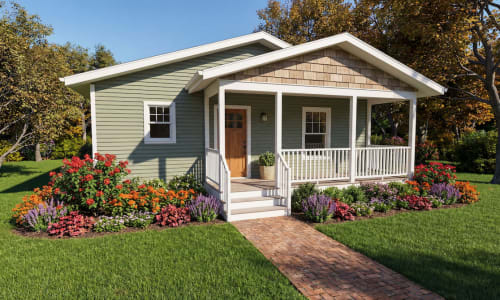 Green cottage-style modular home by Wisconsin Homes featuring a welcoming covered porch with white railings, a wood front door, and a vibrant, colorful flower garden with a brick walkway leading to the entrance.