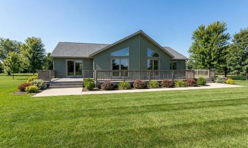 Green cottage-style modular home by Wisconsin Homes in Marshfield, WI with expansive front deck and concrete walkway.