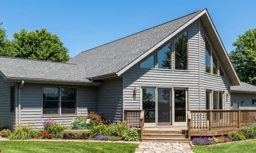 Light gray Chalet-style modular home by Wisconsin Homes in Marshfield, WI with angled roofline and flower-lined deck.