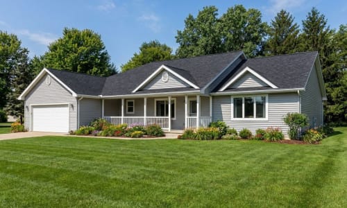 Light gray ranch-style modular home by Wisconsin Homes with white trim, covered front porch, and attached garage in Marshfield, WI.