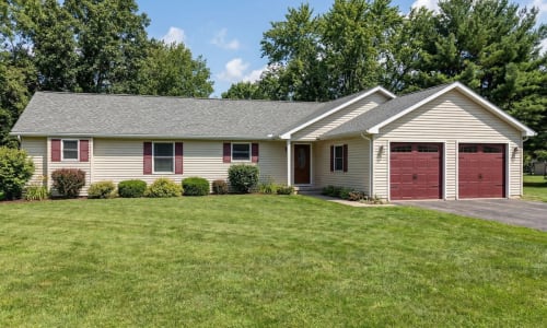Single-story modular ranch home by Wisconsin Homes with tan siding and red garage doors in Marshfield, WI.