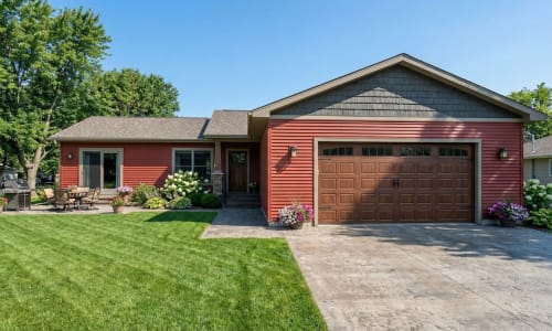 Red cottage-style modular home by Wisconsin Homes in Marshfield, WI with wood garage door and backyard patio.