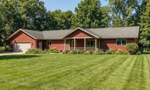 Red ranch-style modular home by Wisconsin Homes with beige trim, front porch, and attached garage in Marshfield, WI.