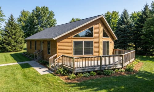 Compact cottage-style modular home by Wisconsin Homes in Marshfield, WI with wood siding and wraparound deck.