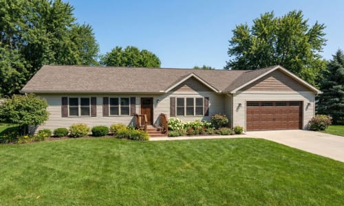 Tan modular home with brown garage door, matching shutters, and landscaped front yard by Wisconsin Homes in Marshfield, WI.