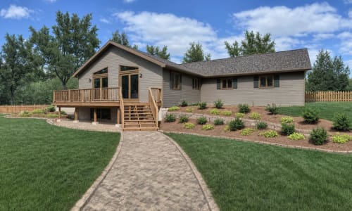 Walkout cottage home by Wisconsin Homes with raised deck, stone walkway, and landscaped garden beds.