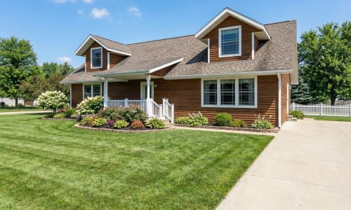 Wood-tone Cape Cod modular home by Wisconsin Homes in Marshfield, WI with front porch and landscaped yard.