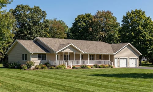 Tan modular ranch home by Wisconsin Homes featuring a wraparound front porch and attached two-car garage in Marshfield, WI.