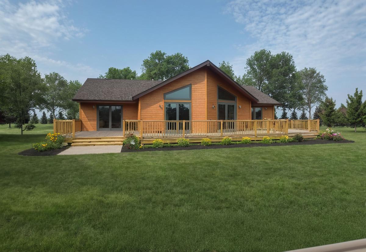 Cedar cottage-style home by Wisconsin Homes with a wraparound wood deck, large windows, and manicured lawn.